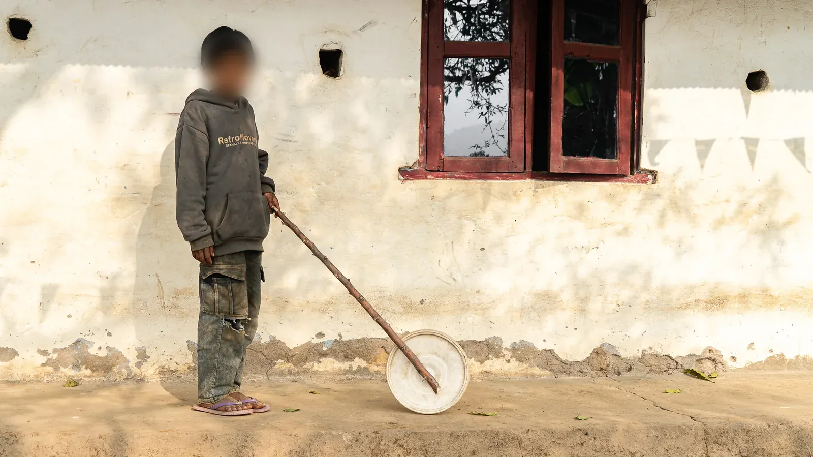 Criança vista de longe num pátio de terra, com o rosto propositalmente desfocado para proteger sua identidade